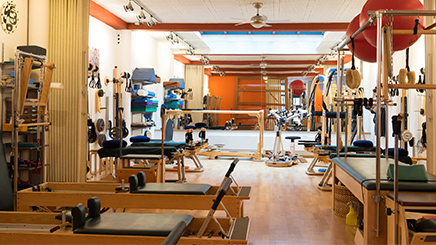 A well-equipped Pilates studio with various exercise machines and equipment arranged neatly in a brightly lit room with wooden floors.