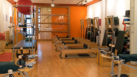 A Pilates studio with reformer machines, a cadillac table, and other exercise equipment on a wooden floor.